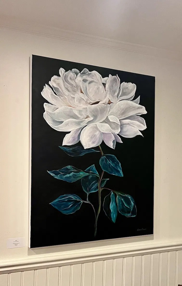 Karen Simon’s large white peony painting with deep teal leaves on a black background, hung on a panelled gallery wall above white wainscoting.