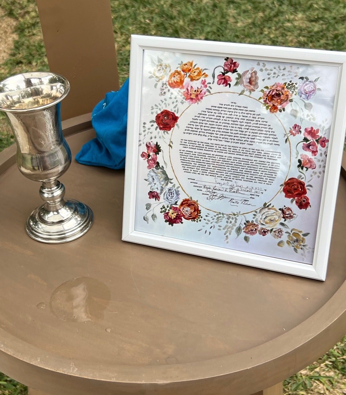 Framed floral ketubah beside a silver kiddush cup