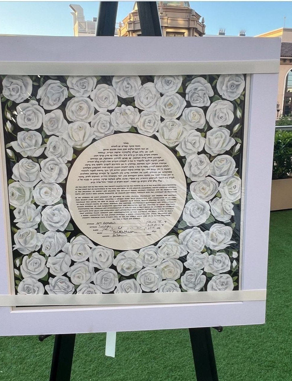 White-rose ketubah displayed on an easel at a wedding