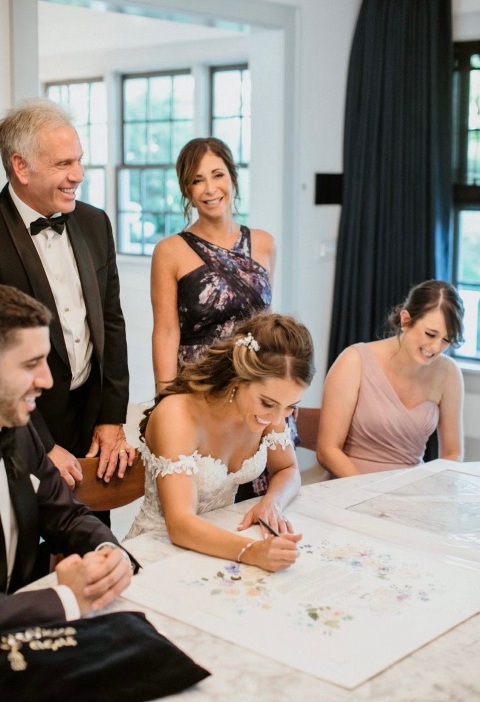 Bride signing her ketubah surrounded by family