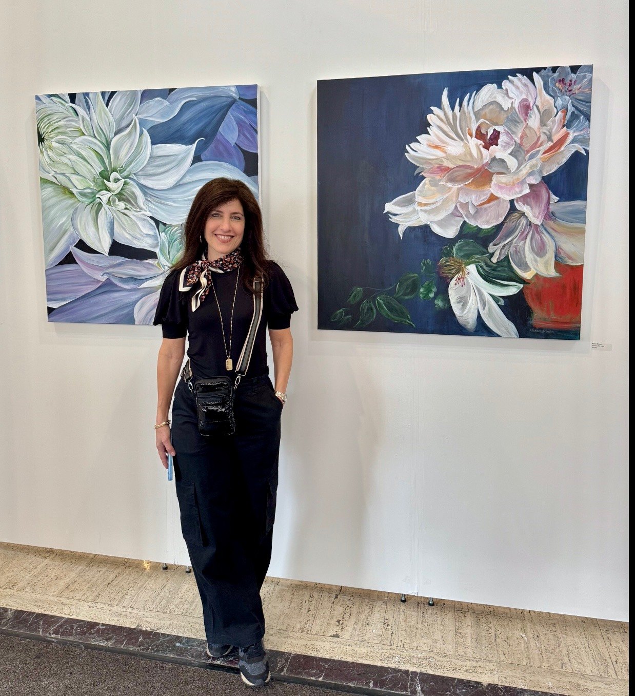 Karen Simon standing with two of her floral paintings at a gallery exhibition